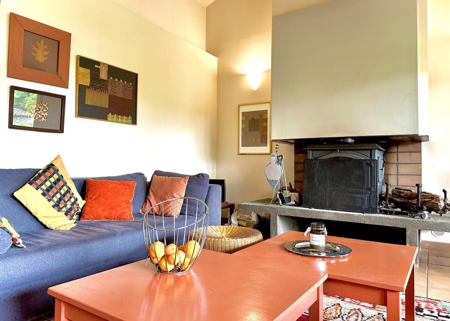 Una sala de estar acogedora con un sofá azul, cojines naranjas, una mesa de centro y una chimenea con leña.