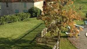 Un bâtiment en pierre avec un toit rouge, entouré d’une pelouse bien entretenue et d’une clôture en bois.