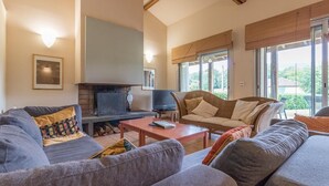 Un salon spacieux doté d’une cheminée, de sièges confortables et de grandes fenêtres offrant une vue sur l’extérieur.