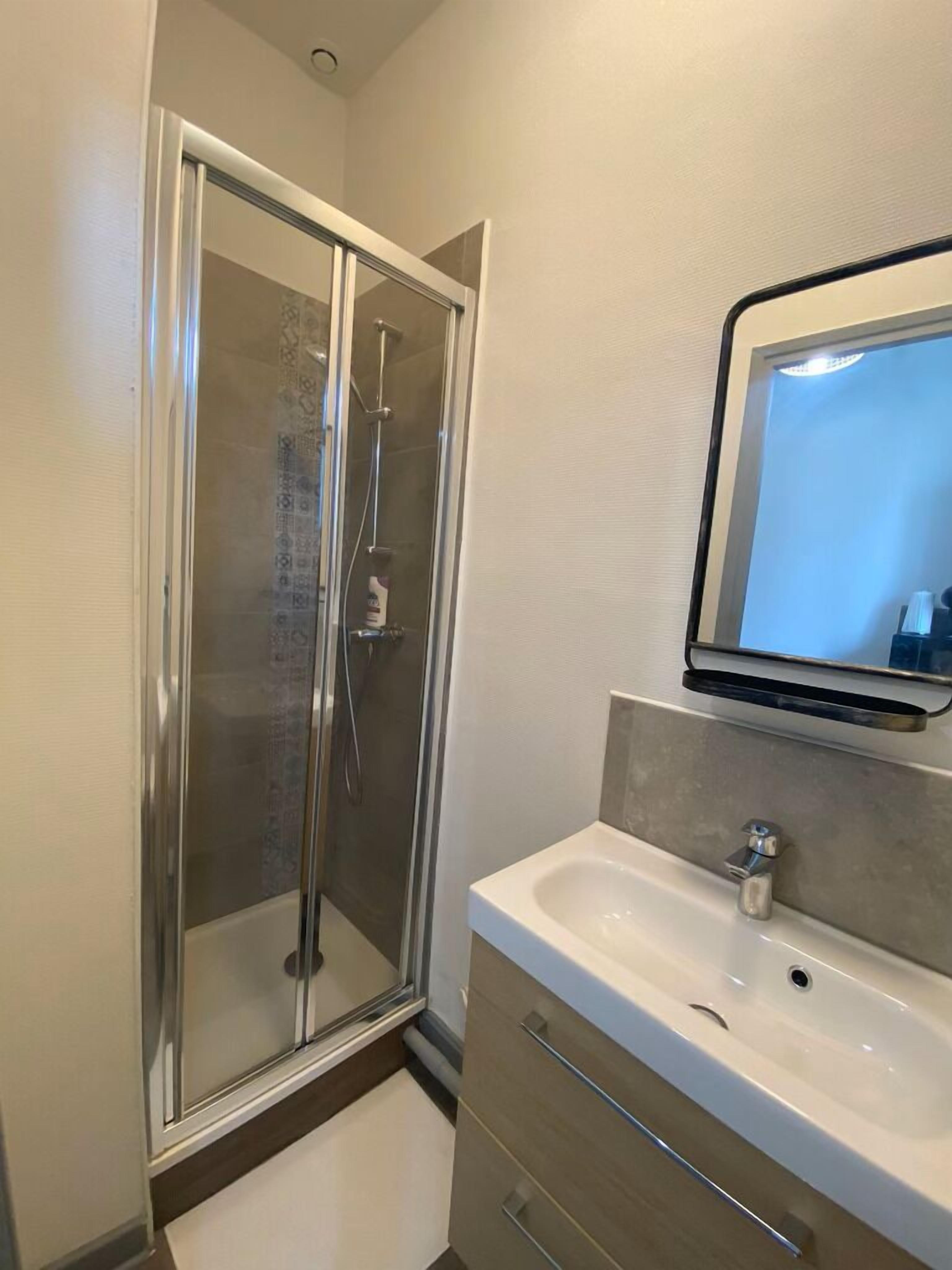 Une salle de bain avec une douche à parois de verre, un lavabo avec un miroir au-dessus et un porte-serviettes.