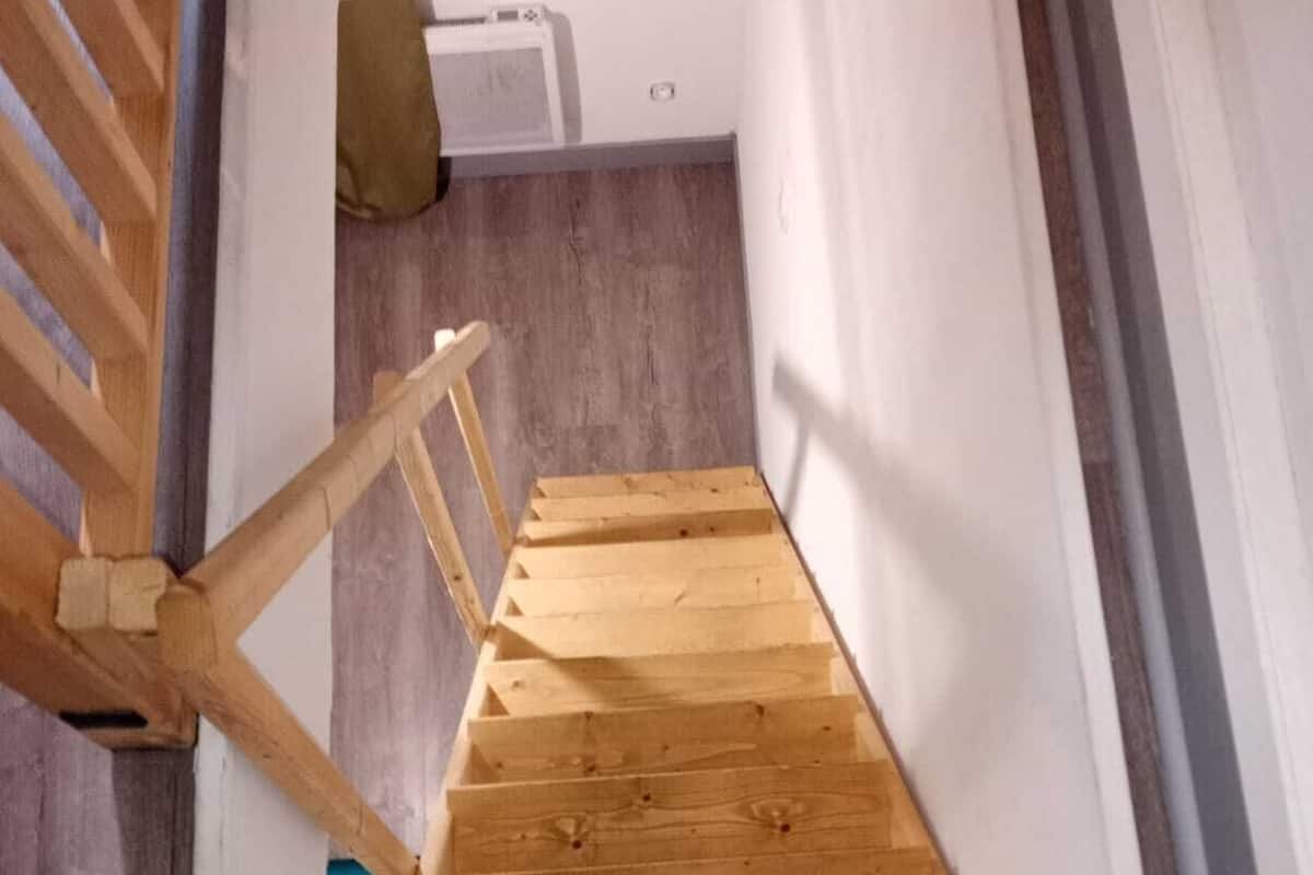 A wooden staircase with a simple design, leading to a room with a white wall and a visible air conditioning unit.