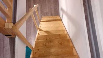 A wooden staircase with a simple design, leading to a room with a white wall and a visible air conditioning unit.