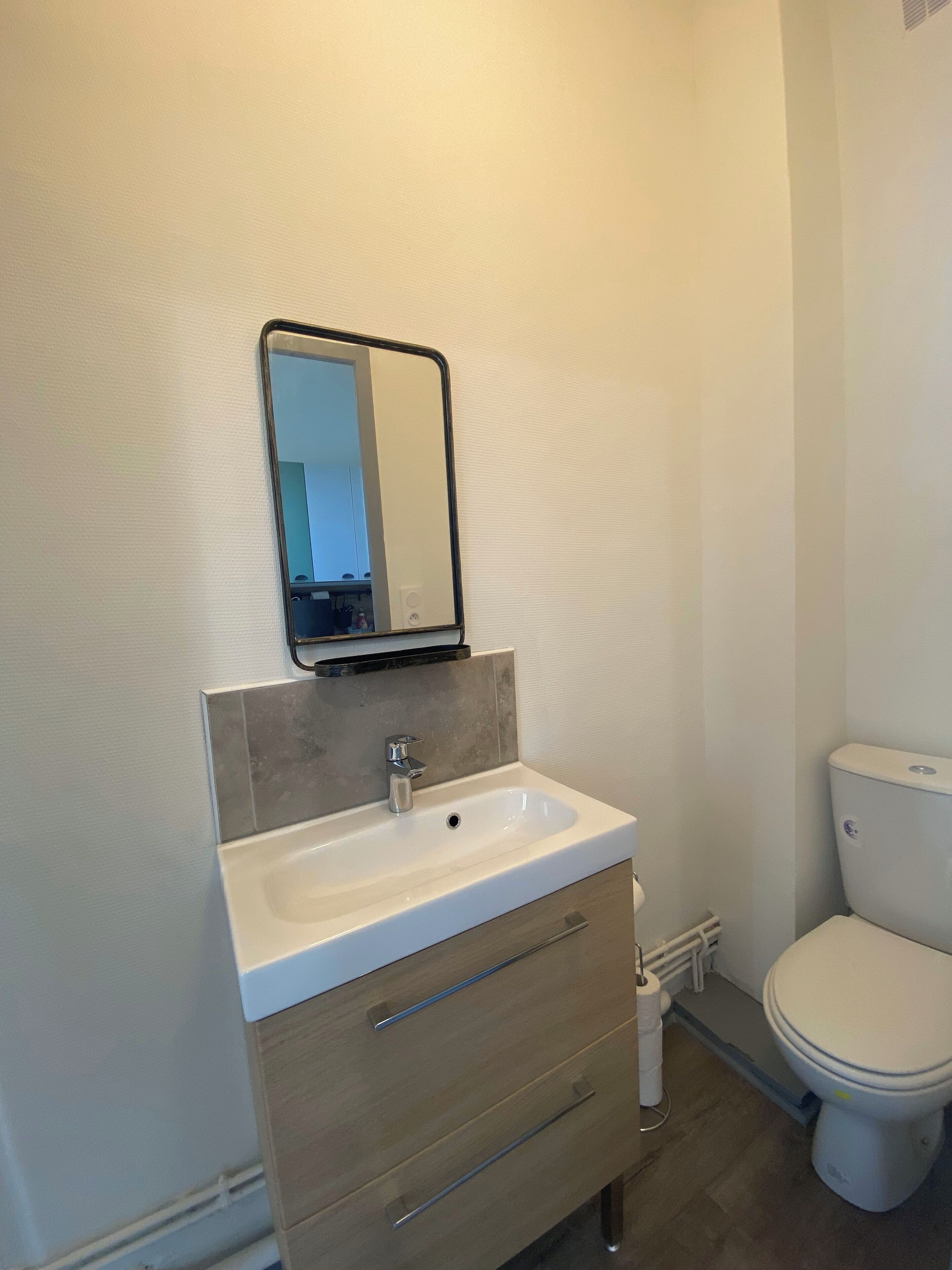 Ein Badezimmer mit einem weißen Waschbecken, einem Spiegel, einer Toilette und Holzschränken.