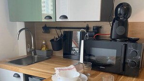 A compact kitchen with a sink, microwave, and coffee maker. There are two stools and a small dining table set with white plates and bowls. - Les Sources Vichy  (Vichy)