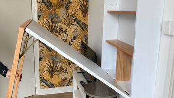 Een kamer met een houten ladder tegen een muur, een wit wandrek en een kleine ronde tafel.