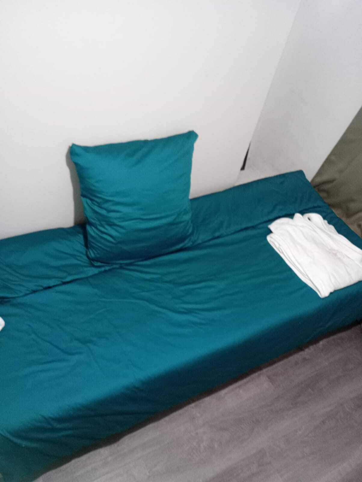 Una cama individual con ropa de cama color turquesa y una almohada blanca.