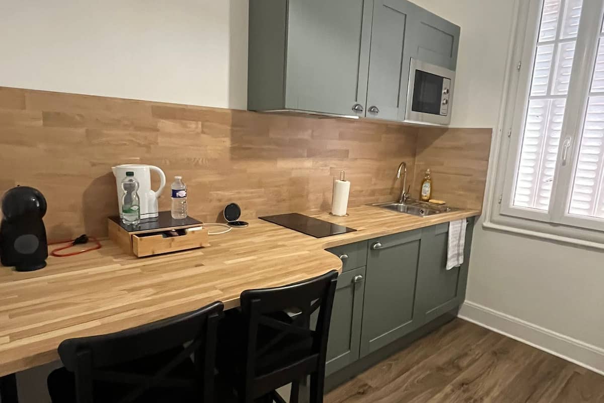 A compact kitchen with a wooden countertop, two black chairs, a microwave, and a hanging light fixture.