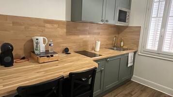 A compact kitchen with a wooden countertop, two black chairs, a microwave, and a hanging light fixture.