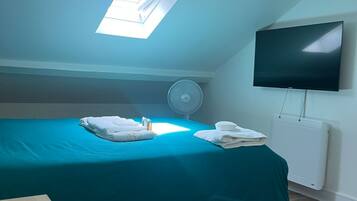 A room with a bed, a TV, a fan, and a skylight.