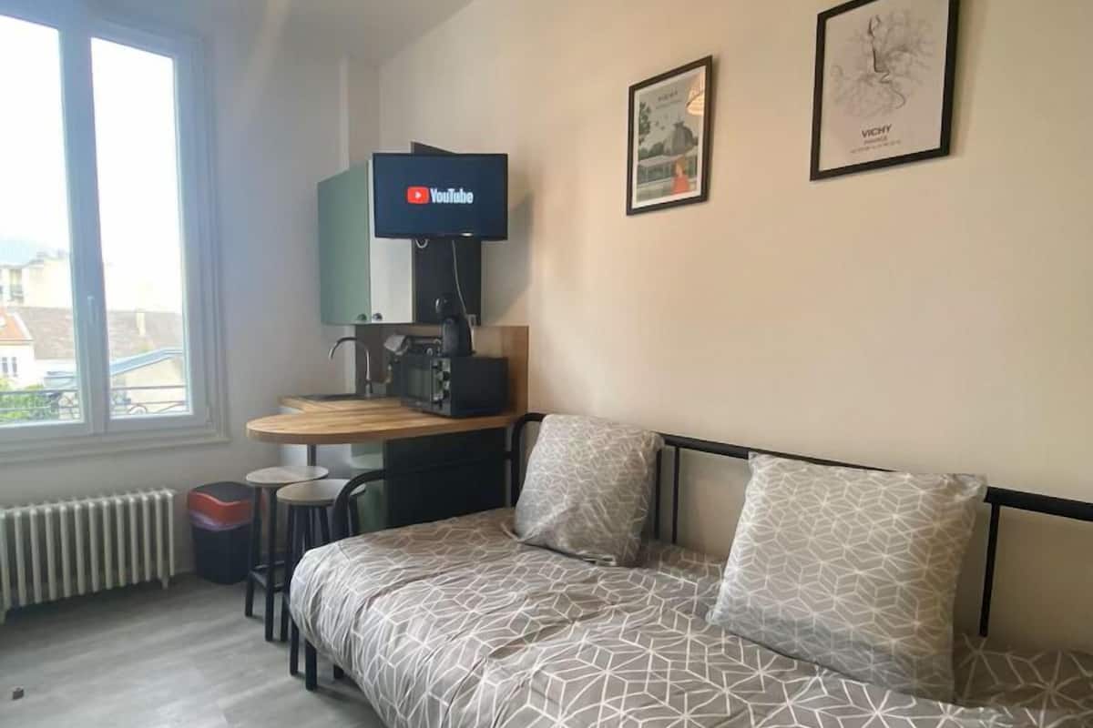 A modern room with a sofa bed, a small desk, a television, and a window with a view.