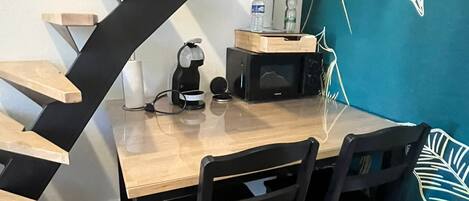 A dining area with a wooden table and chairs, a microwave, and a water dispenser on a teal wall with a leaf pattern.