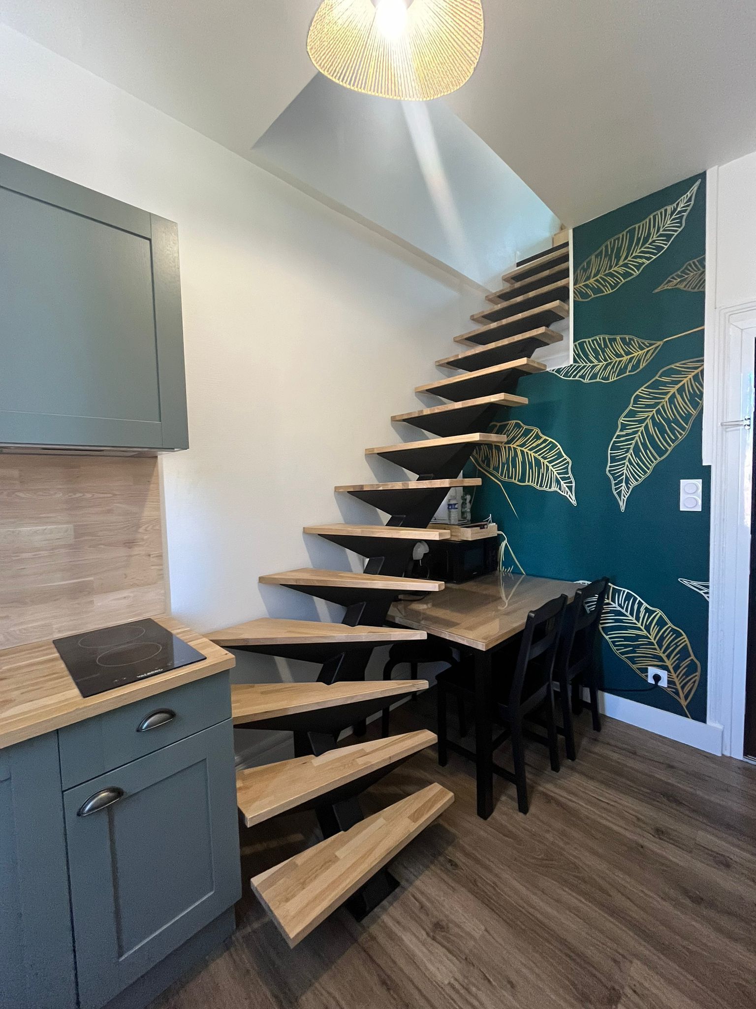 A modern kitchen with a wooden staircase leading to a dining area.