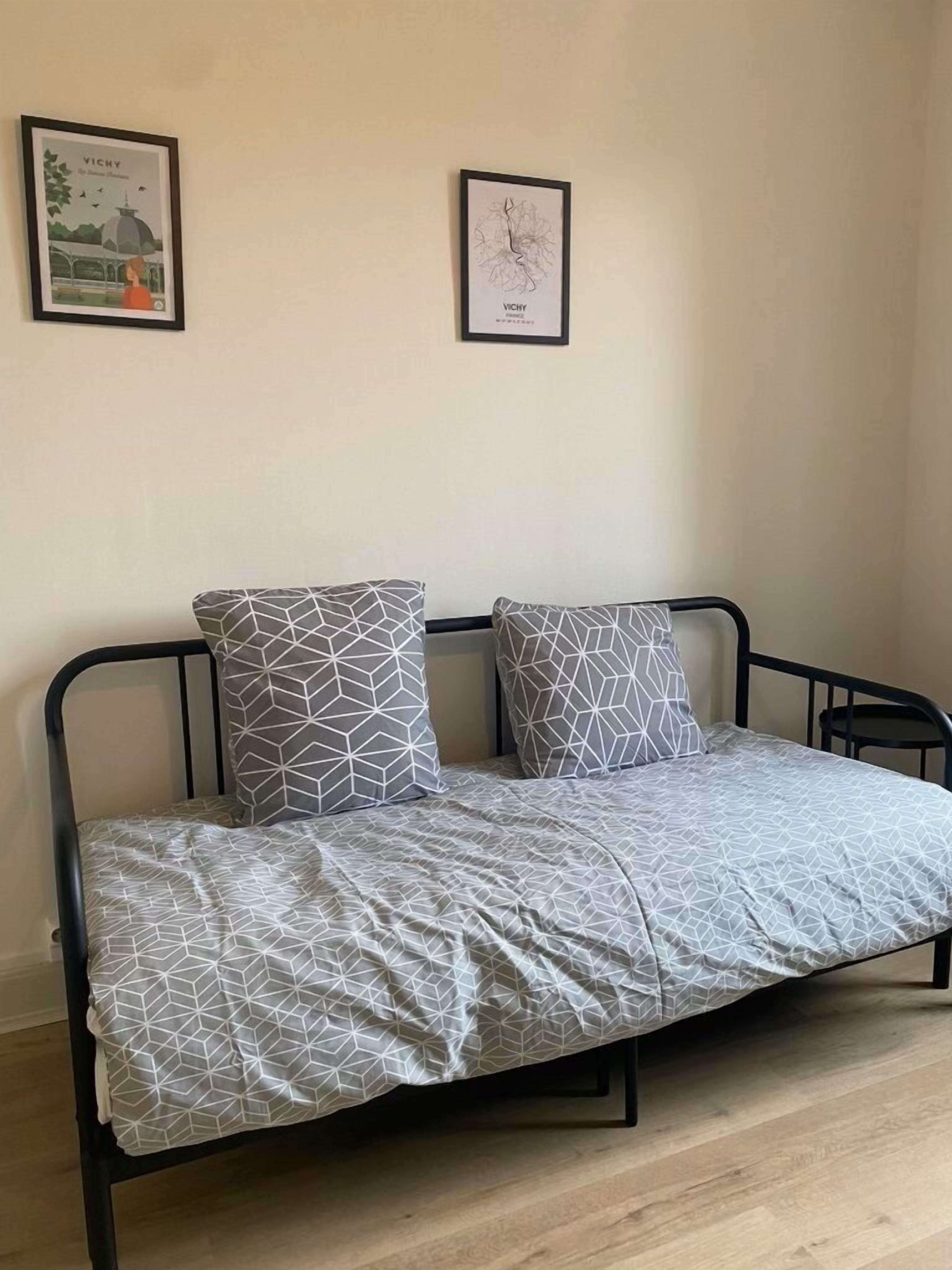 Un lit simple avec une couvre-lit et des oreillers à motifs géométriques, un cadre en métal noir et deux œuvres d’art encadrées accrochées au mur.
