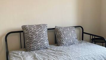 Un lit simple avec une couvre-lit et des oreillers à motifs géométriques, un cadre en métal noir et deux œuvres d’art encadrées accrochées au mur.