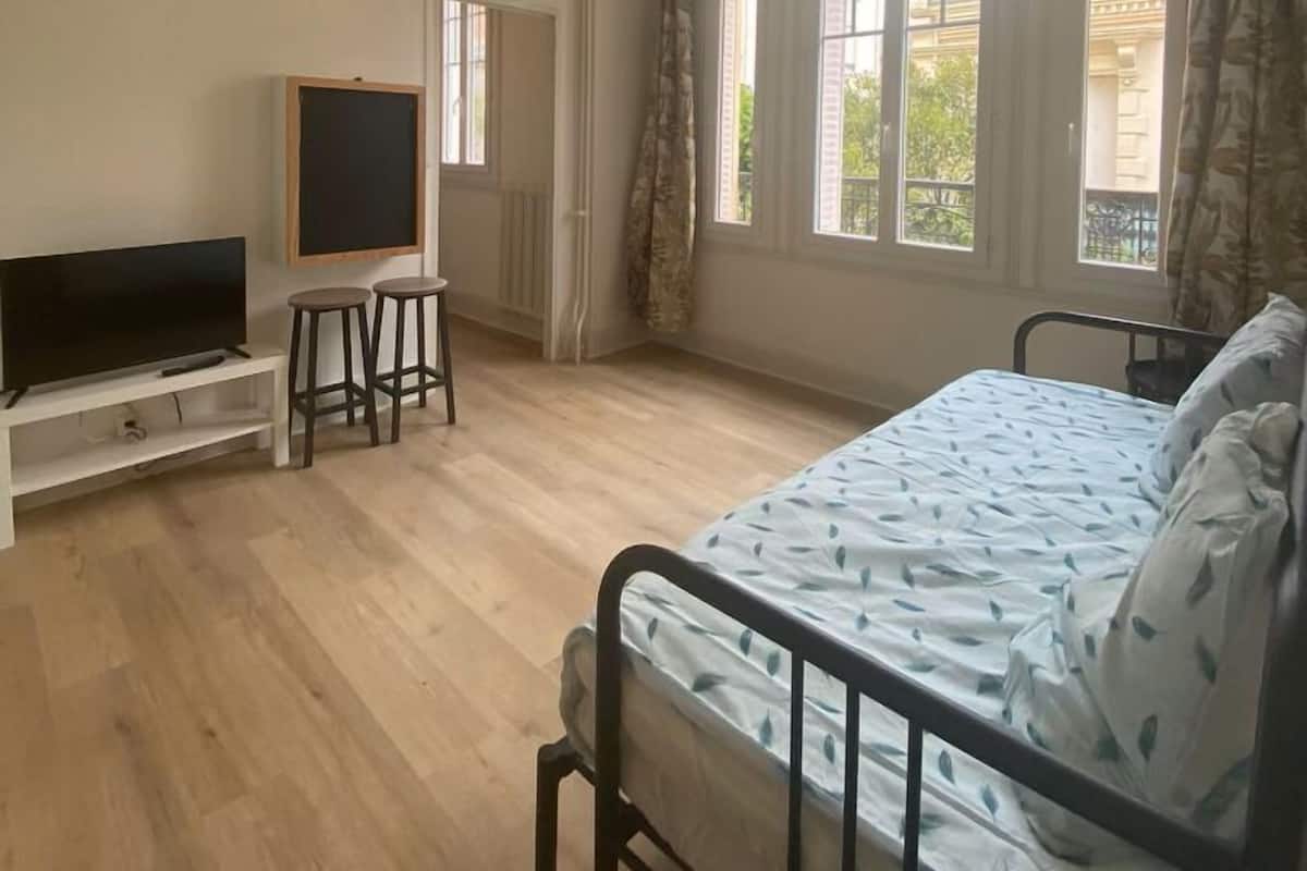 A bedroom with a bed, a TV, a desk, and a window.