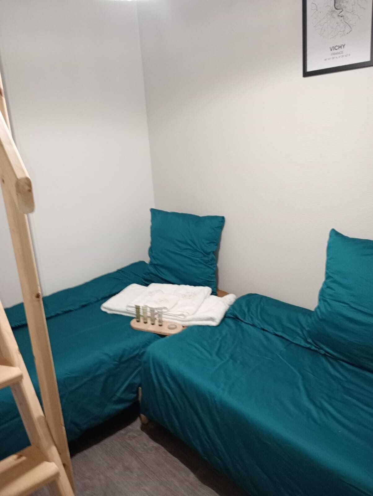 A small room with teal bedding, a wooden ladder, and a framed picture on the wall.