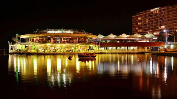 A waterfront building with a glass facade, a boat docked in front, and a large open area with a roof structure. - Les Sources Vichy  (Vichy)