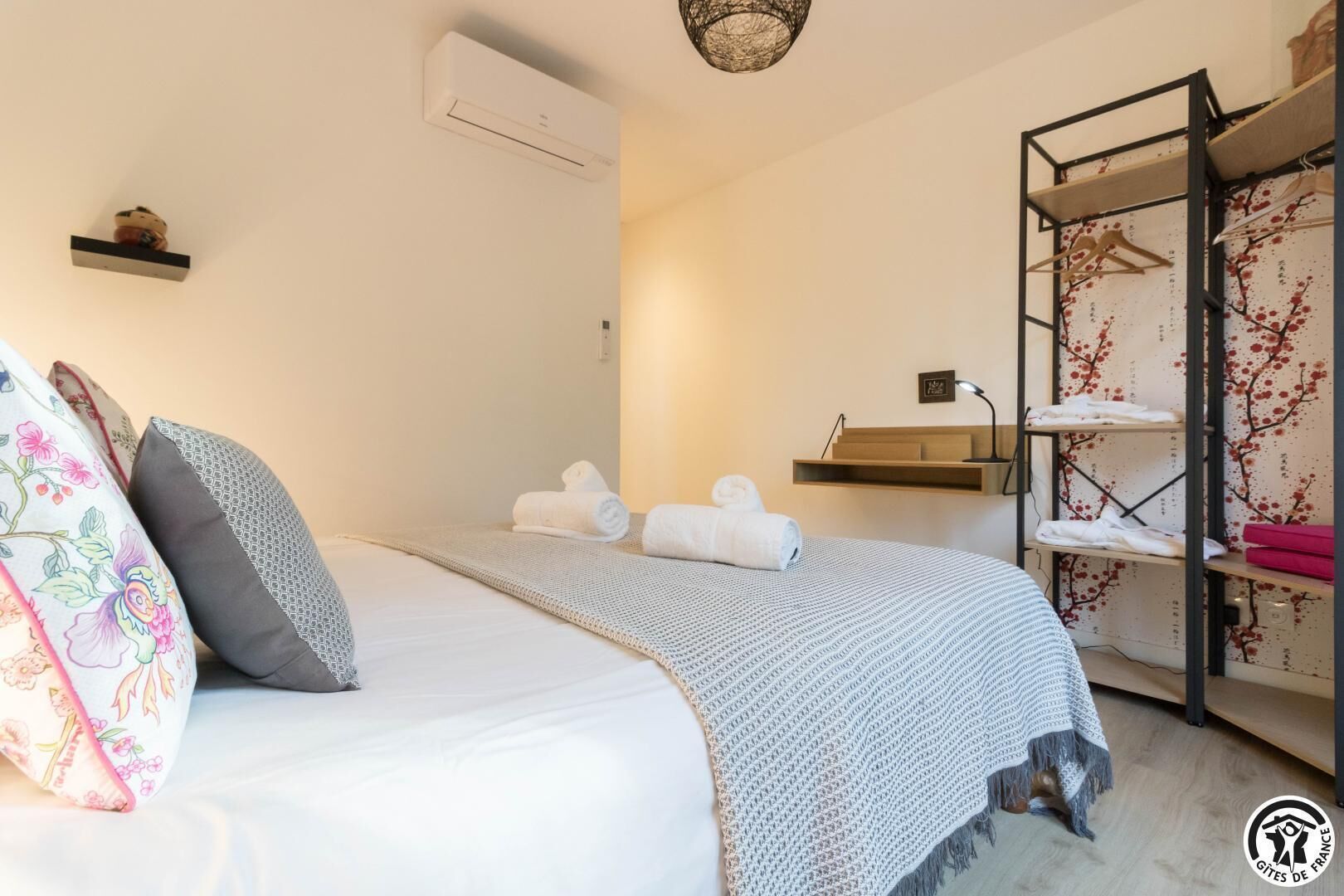 Une chambre à coucher avec un lit, des oreillers, une couverture, un porte-serviettes et une étagère avec des vêtements pliés.