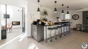 A modern kitchen with a central island, bar stools, pendant lighting, and a clock on the wall. - Villa La Sauzière - BUZET SUR TARN (BUZET SUR TARN)