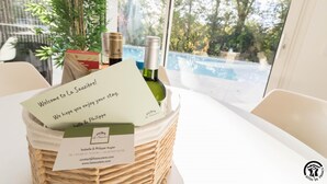 A wicker basket on a table with a welcome note, wine bottles, and a view of a swimming pool through a window. - Villa La Sauzière - BUZET SUR TARN (BUZET SUR TARN)
