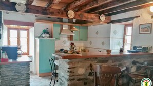 A rustic kitchen with exposed wooden beams, a stone island, and a green and white tiled backsplash. - Chez Marthe - Melles (Melles)