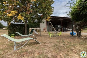Un parque infantil con columpios y un tobogán, una estructura cubierta, y un tractor al fondo.