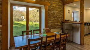 Uma área de refeições com uma mesa e cadeiras de madeira, uma parede de pedra e vista para o exterior.