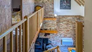 Quarto em estilo loft com vigas de madeira aparentes, parede de pedra e claraboia.
