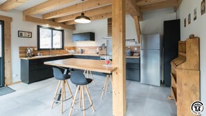 A modern kitchen with wooden beams, a large island, bar stools, and a refrigerator. - Pyrenean chalet Fryo - Poubeau (Poubeau)