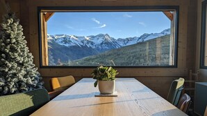 A wooden dining table with a potted plant in the center, a Christmas tree to the left, and a mountain view through a large window. - Pyrenean chalet Fryo - Poubeau (Poubeau)