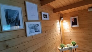 Un intérieur en bois, avec des tableaux encadrés accrochés au mur, une petite table ornée de plantes et un luminaire au plafond.