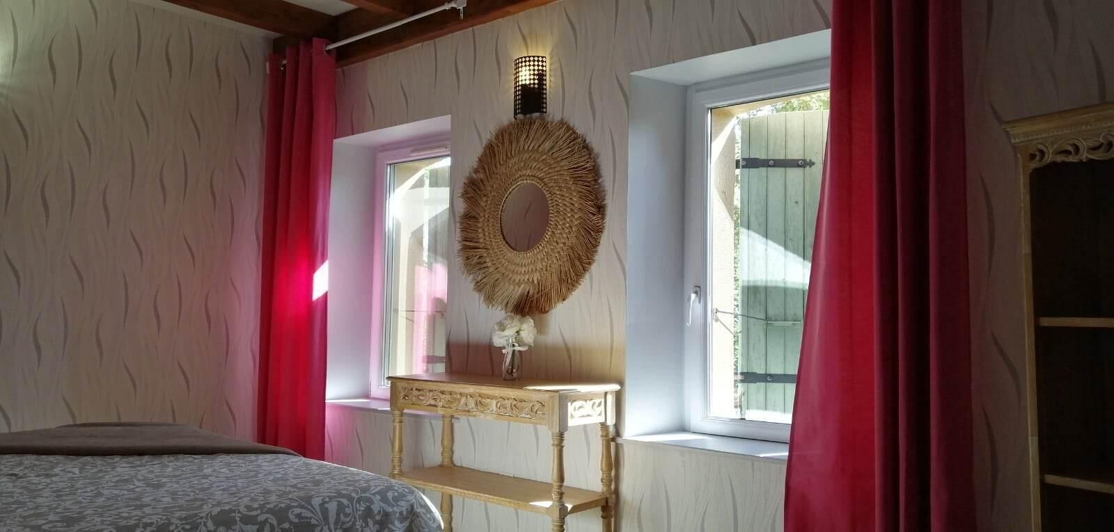 Ein Schlafzimmer mit Bett, Nachttisch, Spiegel und einem Fenster mit Vorhängen.