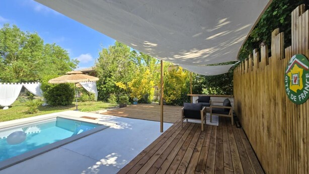 Une terrasse en bois avec une piscine, du mobilier d’extérieur et un espace abrité orné d’un logo sur le mur.