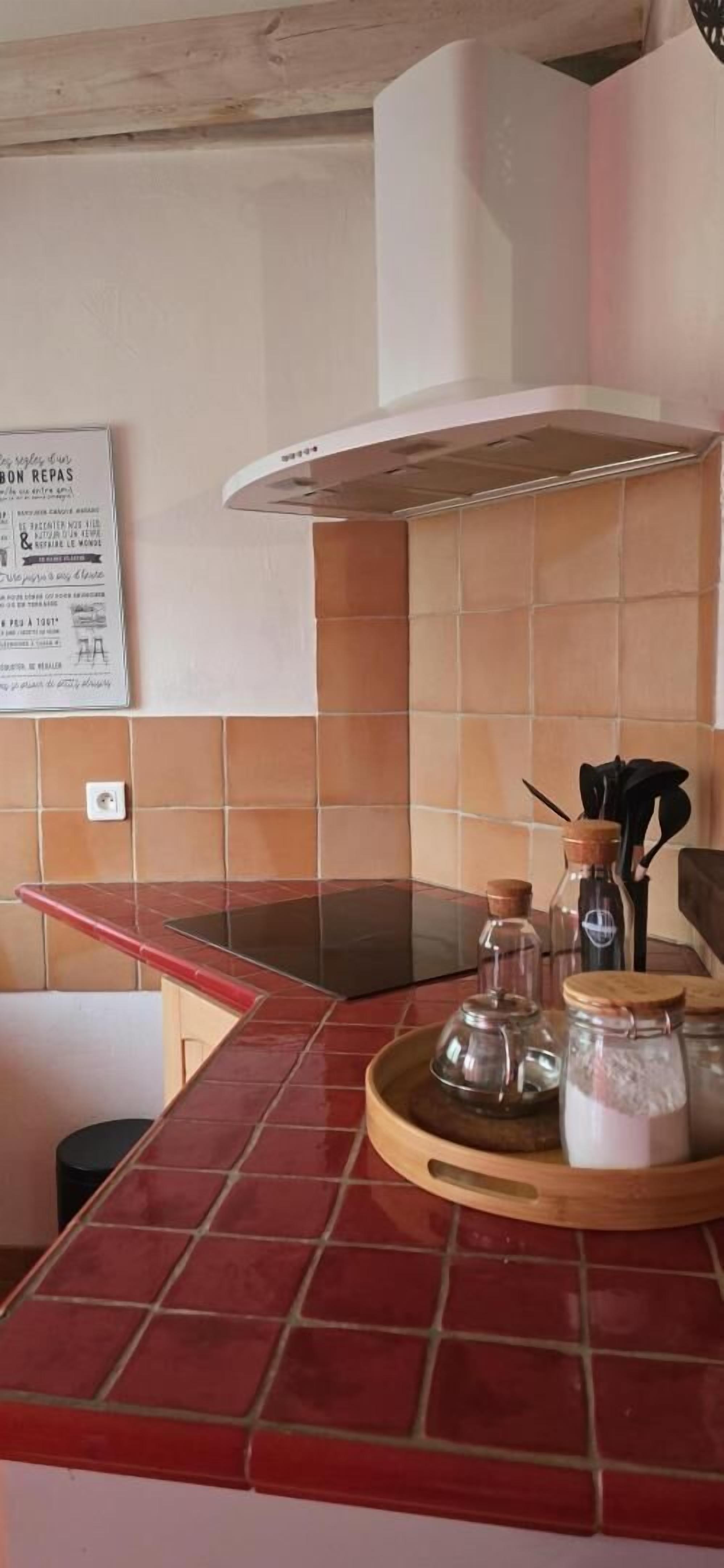Una cocina con encimeras de baldosas rojas, una campana extractora blanca y frascos de vidrio sobre una bandeja de madera.