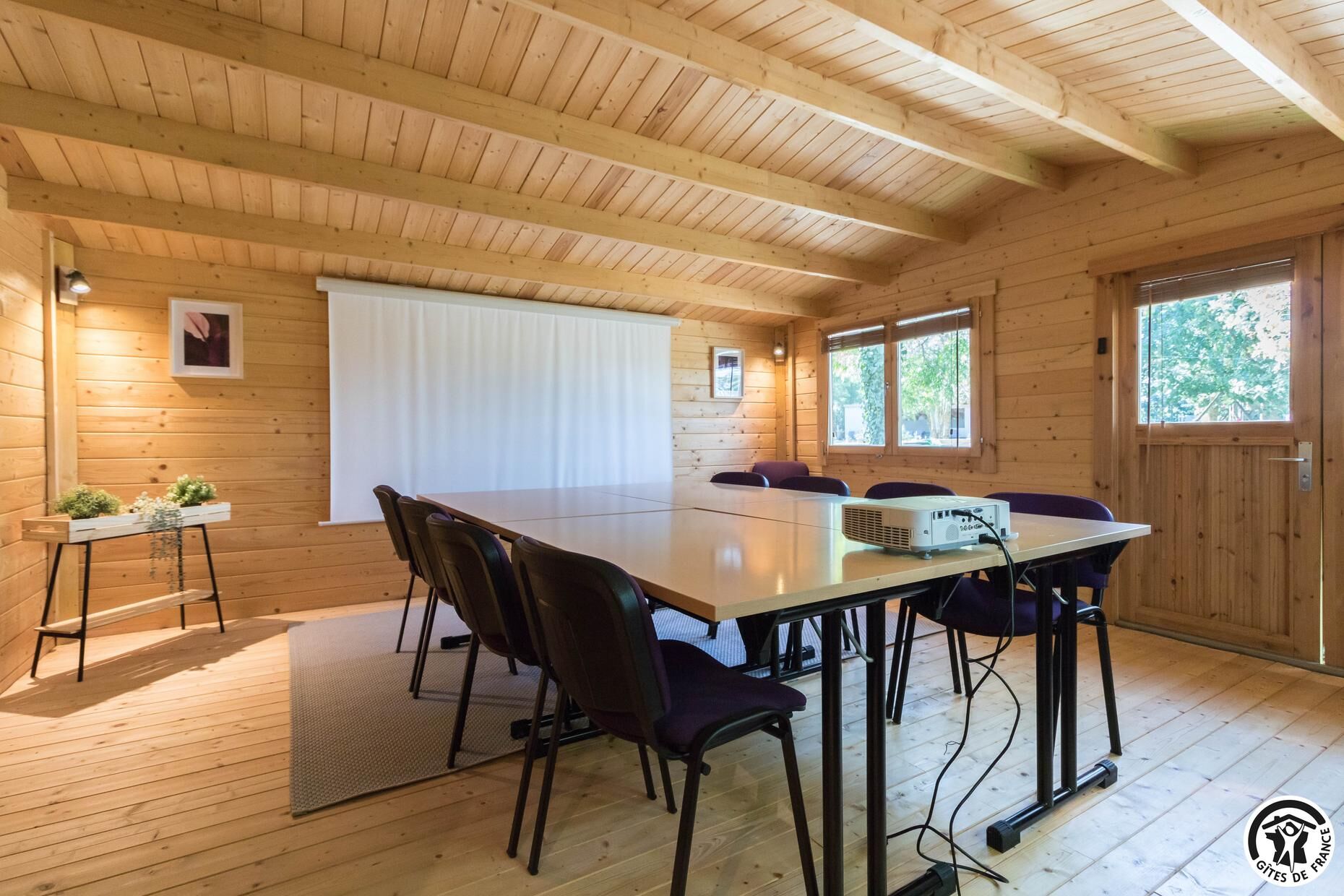 A wooden cabin with a large dining table, chairs, and a projector.