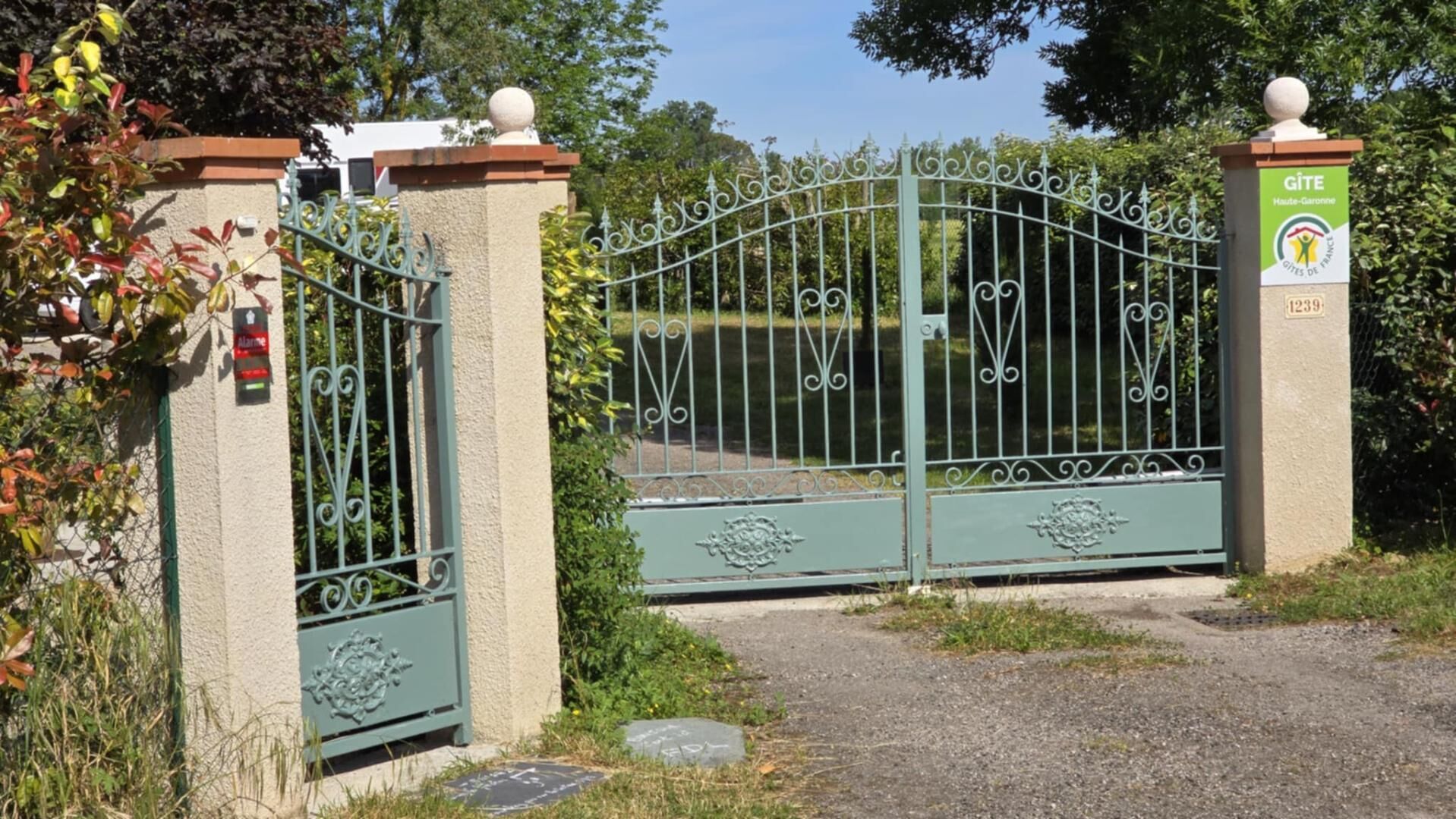 Een omheind toegangspunt met een metalen hek, een groen bord met 'GITE Haute-Garonne' en 'CITIES DE FRANCE' erop, en een klein bord met het nummer '1239'.