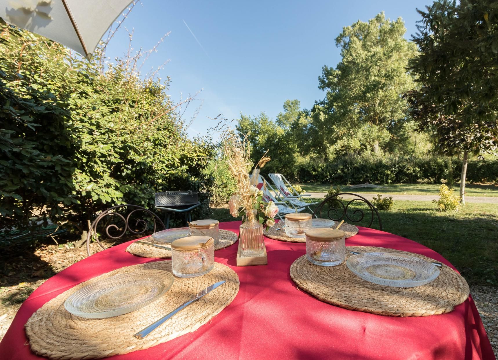 An outdoor dining setup with woven placemats, glassware, and a red tablecloth.