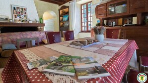 A cozy dining area with a table set for two, featuring a red and white checkered tablecloth, a lace table runner, and a variety of books and magazines.