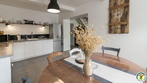 A modern kitchen with white cabinets, a black pendant light, and a rustic wooden wall clock. - Gîte de Pene Blanque - Arbas (Arbas)