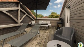 A wooden deck with a black umbrella, a barbecue grill, and outdoor seating. - Gîte de Pene Blanque - Arbas (Arbas)