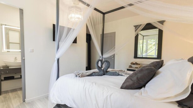 A modern bedroom with a large bed, a bedside table, a mirror, and a window. - Gîte de Pene Blanque - Arbas (Arbas)