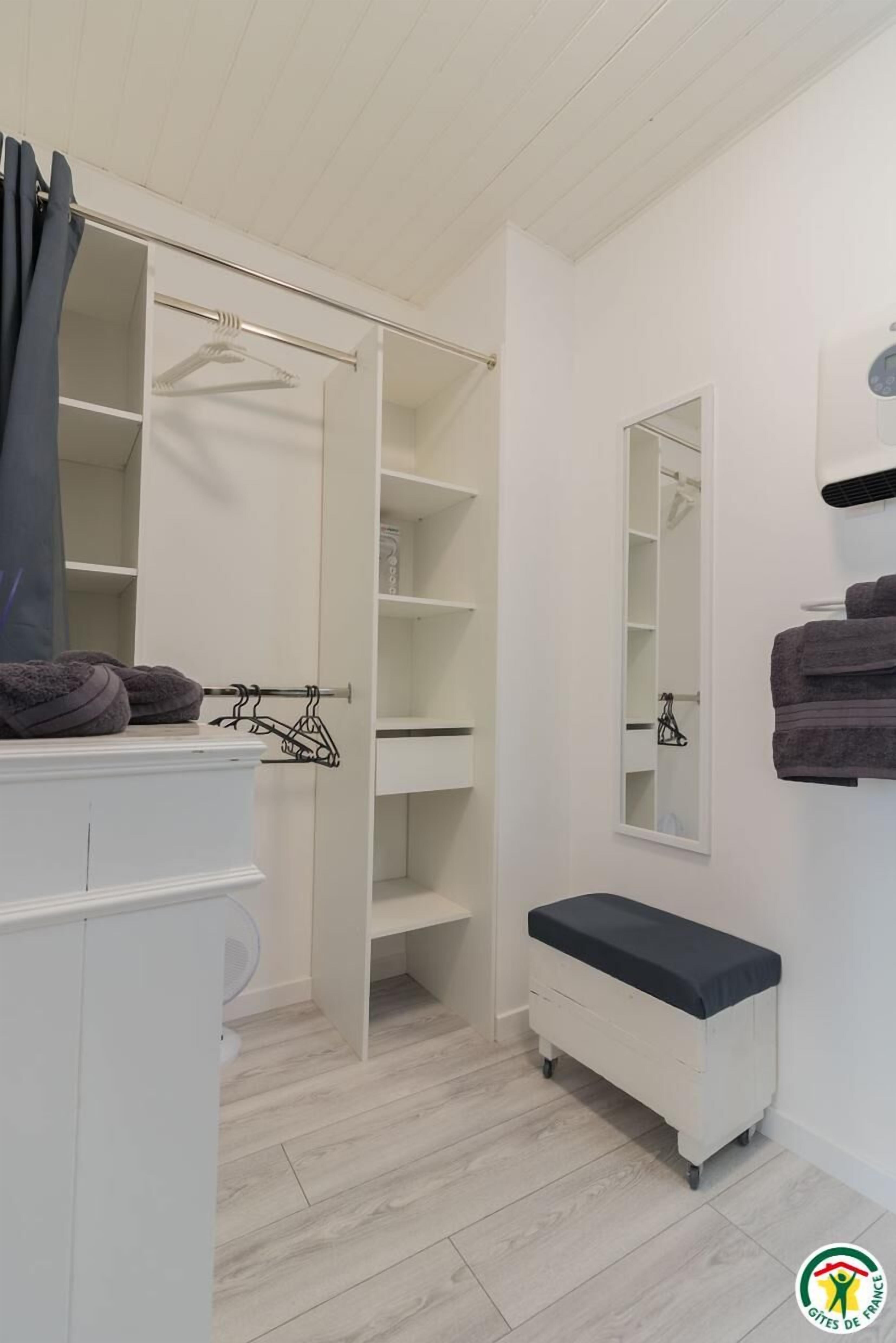 Een witte badkamer met inloopkast, een bankje en een spiegel.