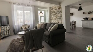 A modern living room with a sofa, a television, and a stone wall. - Gîte de Pene Blanque - Arbas (Arbas)