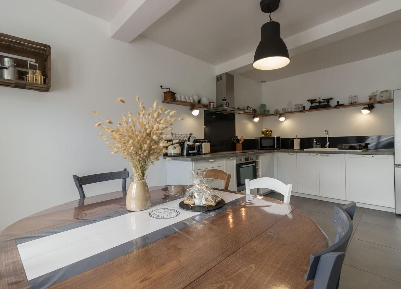 A modern kitchen with white cabinets, a wooden dining table, and a hanging light fixture.