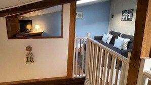 Una habitación con techo de madera, un televisor sobre una estantería, un sofá con cojines y una mesita con lámpara.