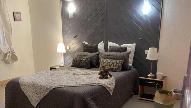Un dormitorio con una cama grande, dos mesitas de noche, una mesita auxiliar, un osito de peluche y una alfombra.