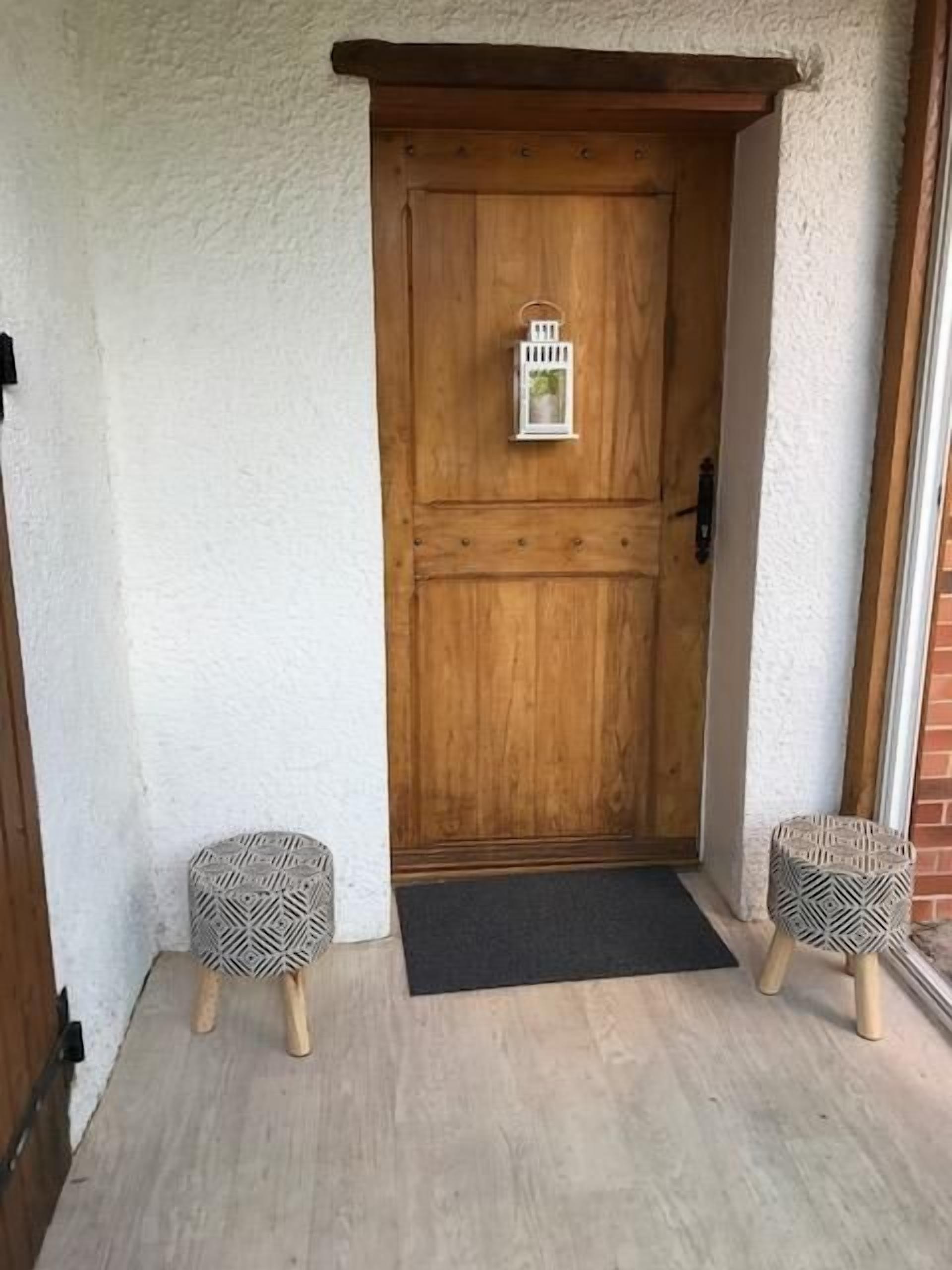 Een houten deur met daarboven een lantaarn, aan weerszijden omringd door twee gestreepten krukken.