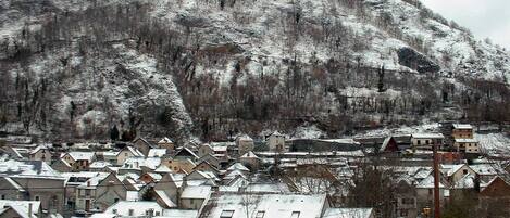 Un village enneigé, avec des maisons regroupées autour d’une place centrale, une église et une montagne en arrière-plan.
