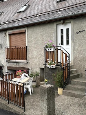 Una casa con balcón, una puerta y una pequeña mesa con sillas.