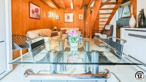 A wooden interior with a glass dining table, sofas, and a staircase.